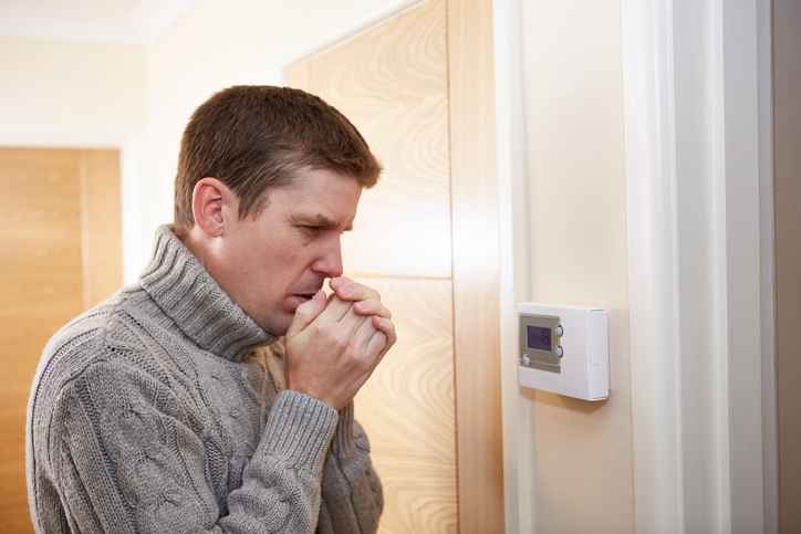 Homeowner standing in front of thermostat freezing