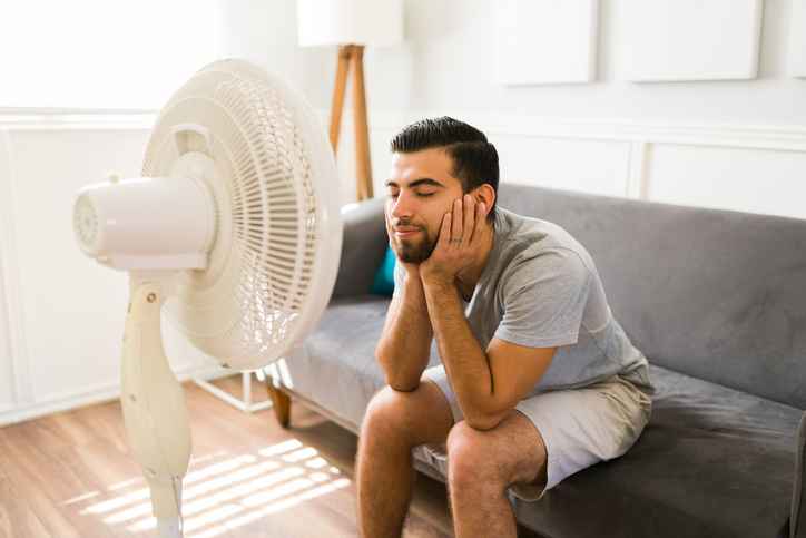 Adult man feeling better at home while relaxing in front of the electric fan during a bad heat wave