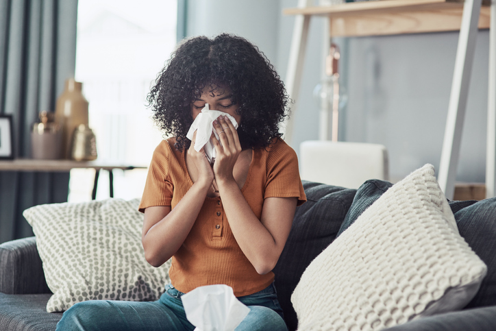 Shot of a young woman blowing her nose with a tissue at home